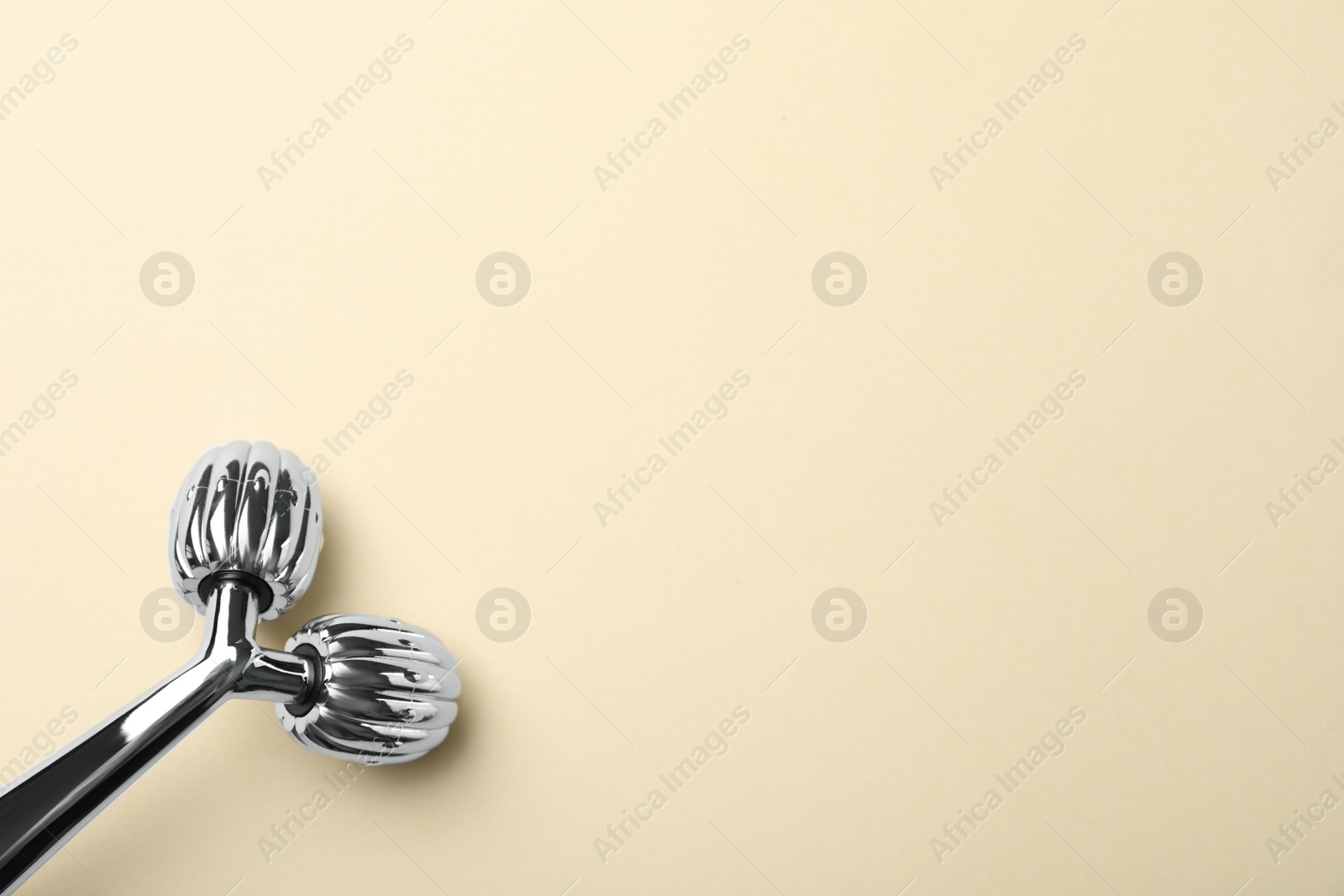 Photo of Metal face roller on beige background, top view. Space for text