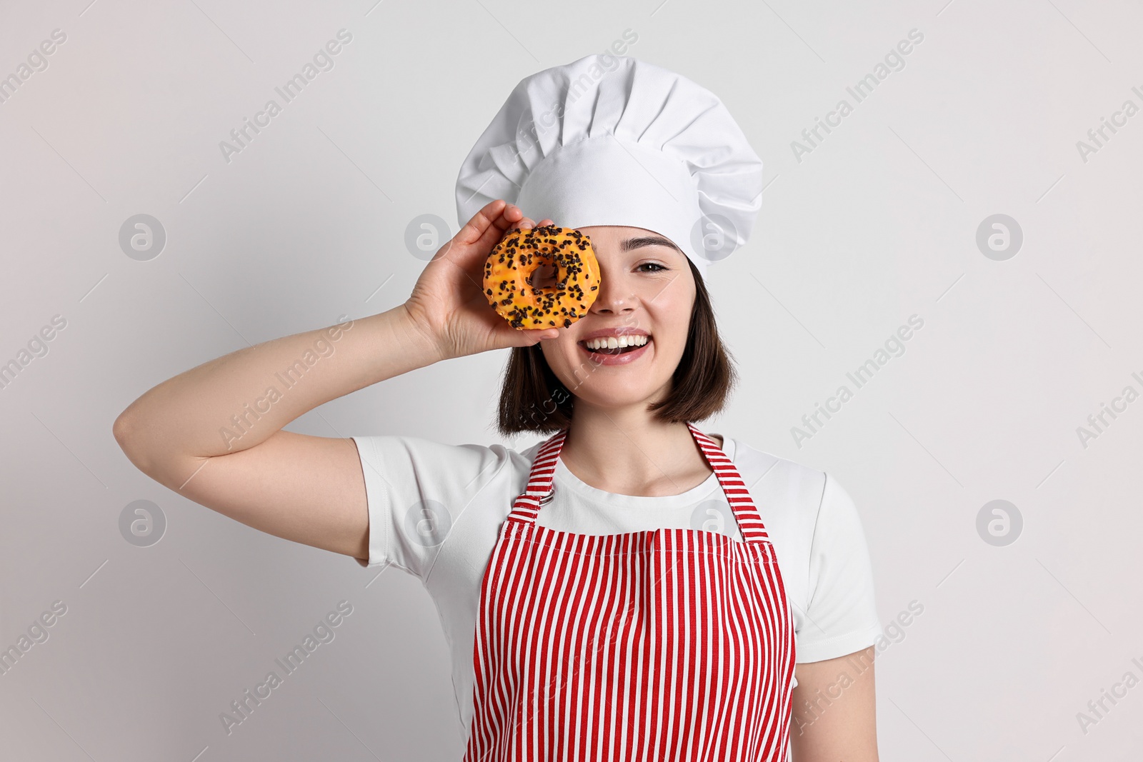 Photo of Happy confectioner with donut on light grey background