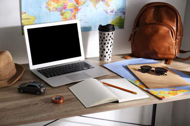 Laptop, notebook and travel accessories on wooden table. Planning summer vacation trip