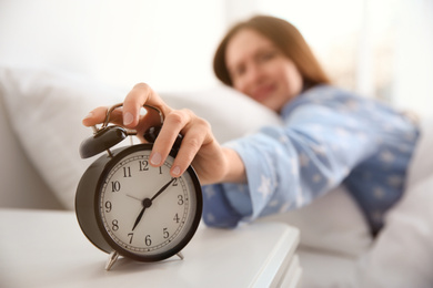 Young woman turning off alarm clock at home in morning, focus on hand