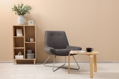 Photo of Living room interior with comfortable armchair, coffee table and shelving unit near beige wall indoors