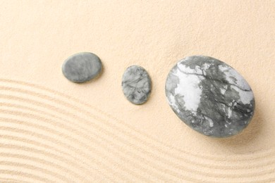 Photo of Zen garden stones on beige sand with pattern, flat lay