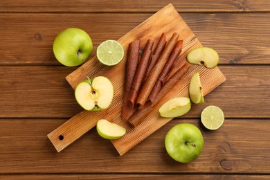 Photo of Delicious fruit leather rolls, apples and limes on wooden table, flat lay