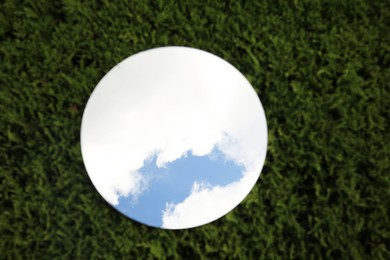 Photo of Round mirror on green grass reflecting cloudy sky, top view