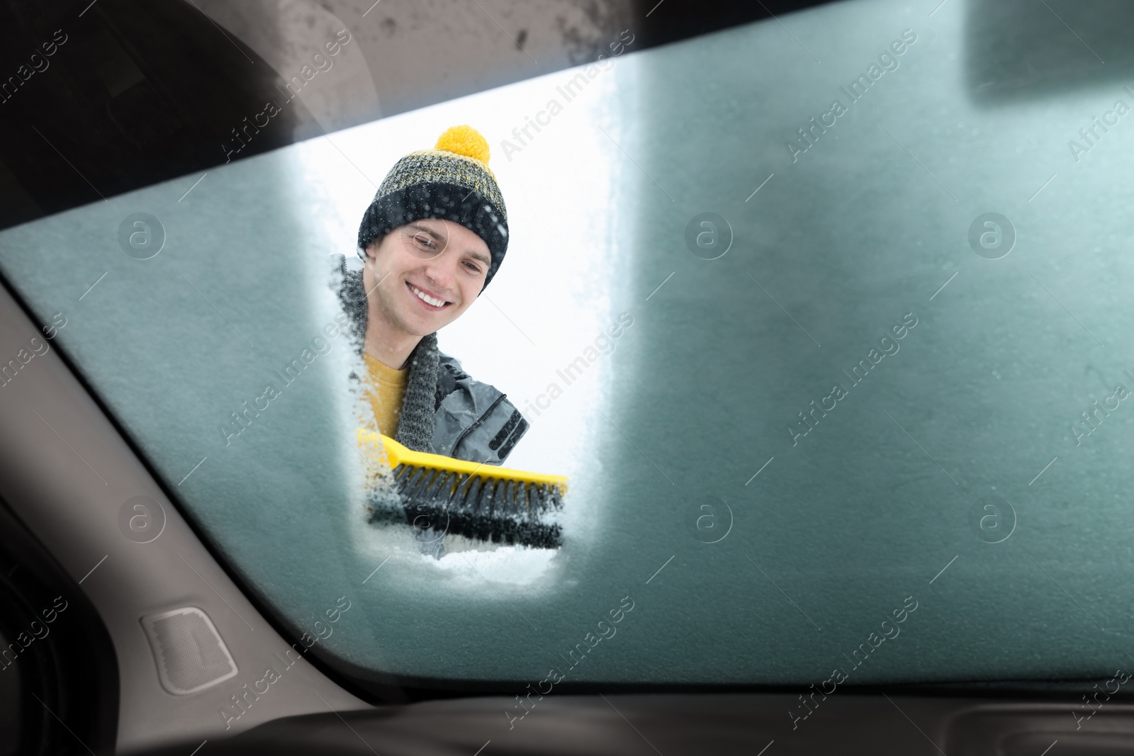 Photo of Man cleaning snow from car windshield, view from inside