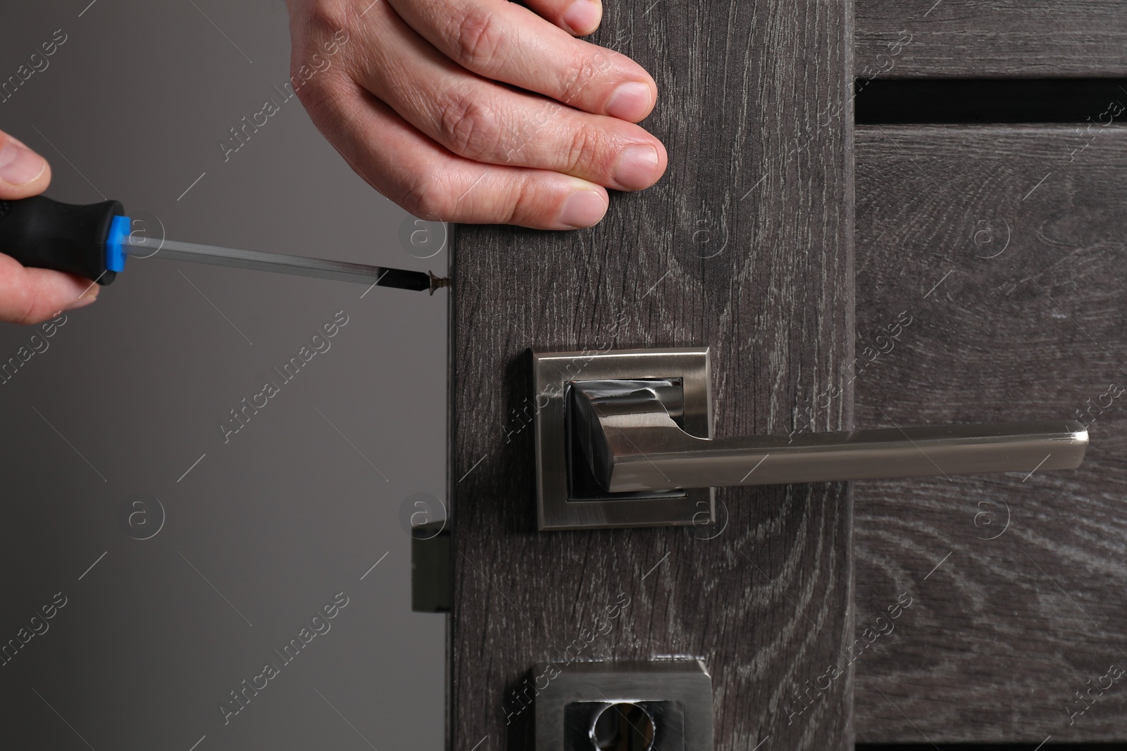 Photo of Handyman with screwdriver repairing door handle indoors, closeup