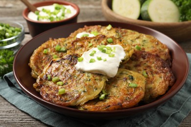 Photo of Delicious zucchini pancakes with sour cream served on wooden table, closeup