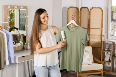 Photo of Young woman cleaning clothes with adhesive lint roller indoors