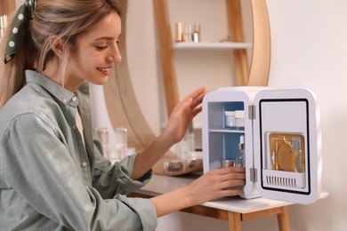Photo of Woman taking cosmetic product from mini fridge indoors