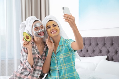 Young friends with facial masks taking selfie in bedroom at pamper party
