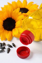 Photo of Bottle of cooking oil, sunflowers and seeds on white table, closeup