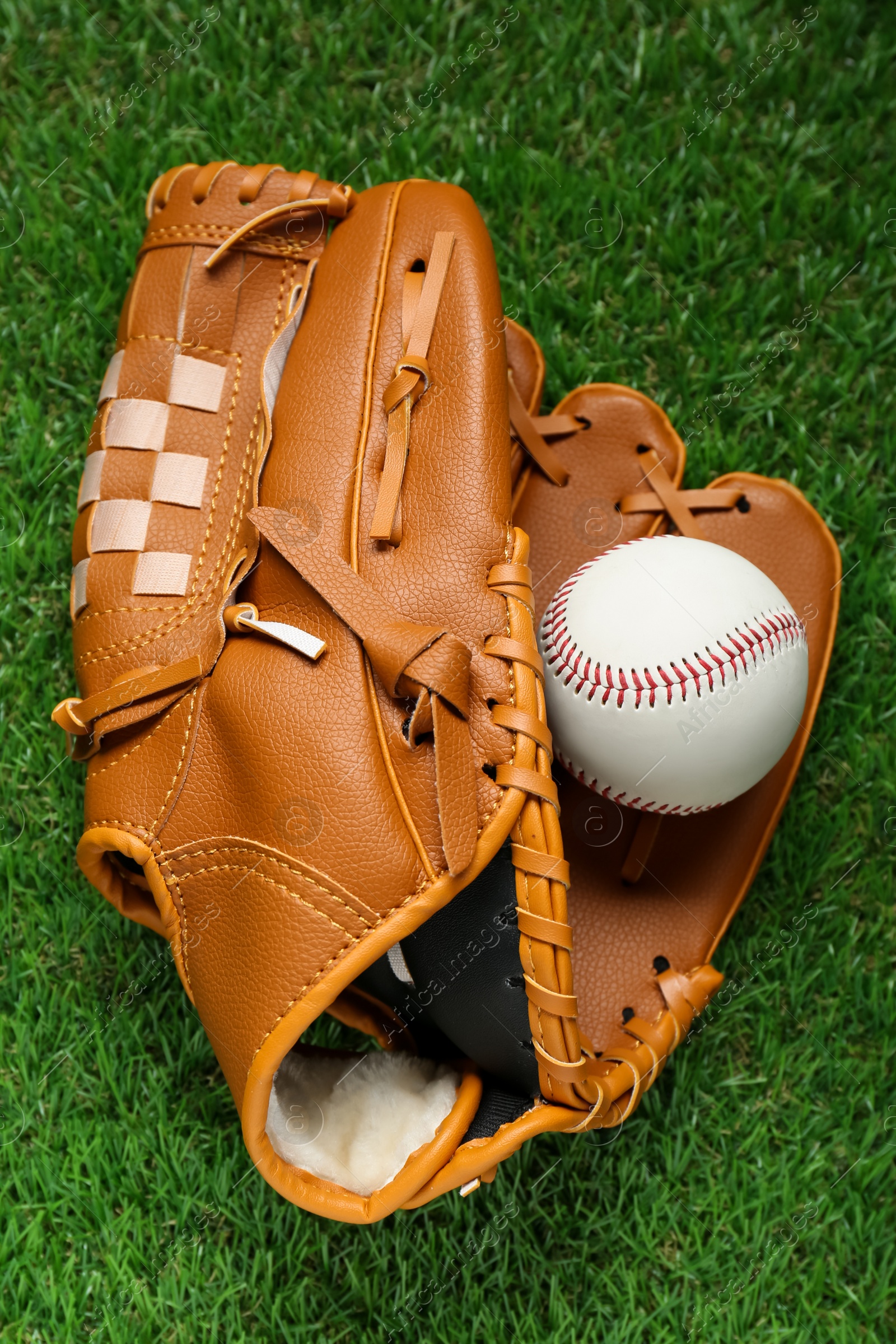 Photo of Catcher's mitt and baseball ball on green grass, top view. Sports game