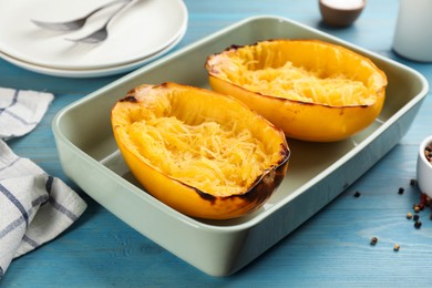 Photo of Halves of cooked spaghetti squash in baking dish on turquoise wooden table, closeup