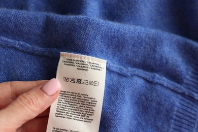 Photo of Woman holding clothing label in different languages on blue garment, closeup