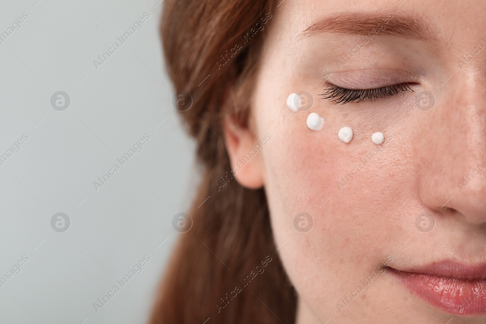 Photo of Beautiful woman with freckles and cream on her face against grey background, closeup. Space for text