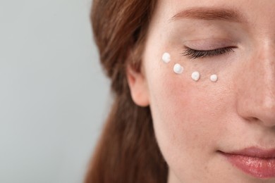 Photo of Beautiful woman with freckles and cream on her face against grey background, closeup. Space for text