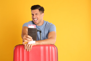 Handsome man with suitcase and ticket in passport for summer trip on yellow background. Vacation travel