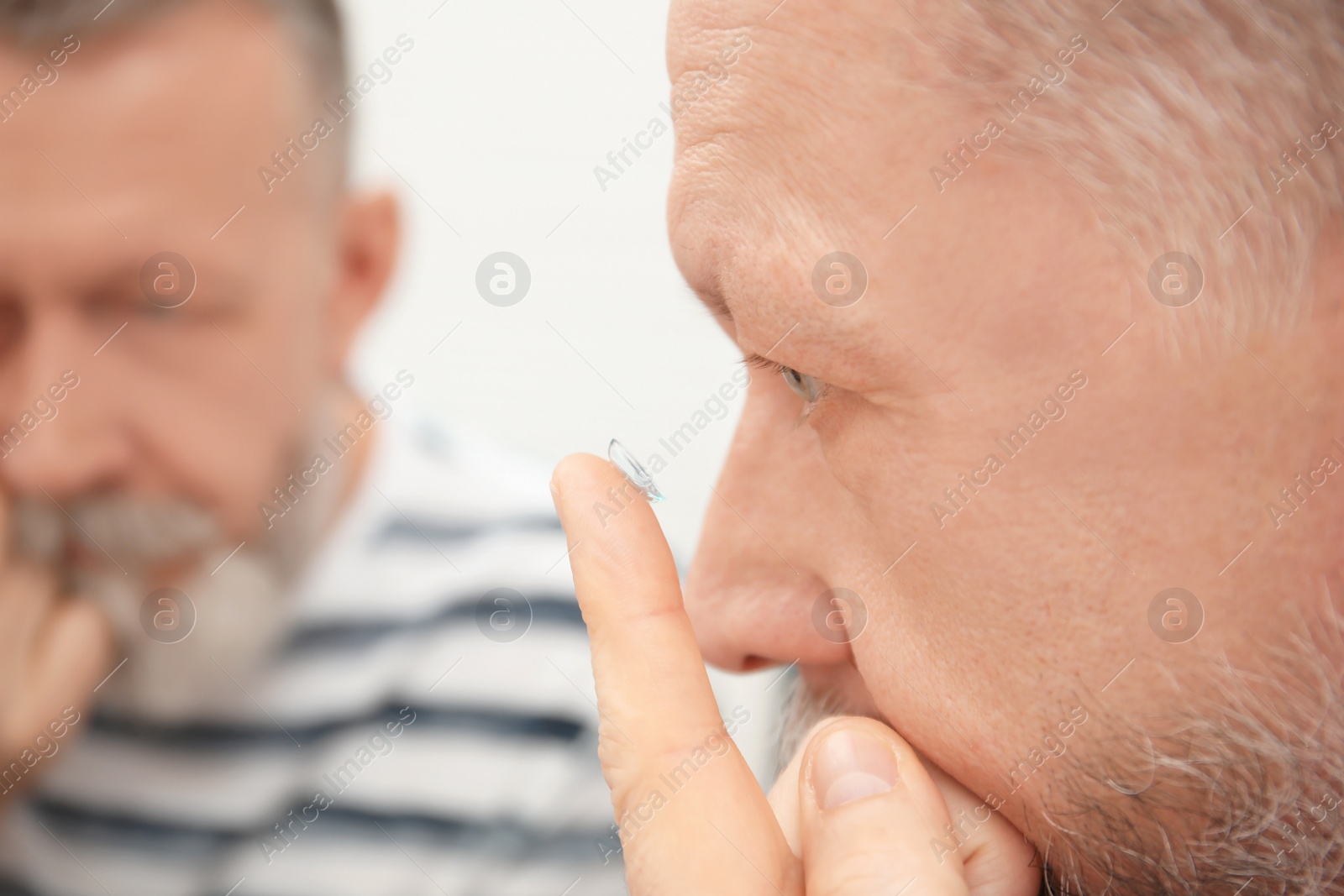 Photo of Senior man putting contact lens in his eye indoors