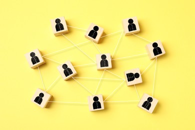 Image of Teamwork. Wooden cubes with human icons linked together symbolizing cooperation on yellow background, top view