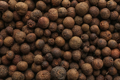 Photo of Allspice peppercorns as background, top view. Aromatic spice