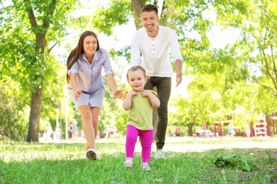 Parents supporting their baby daughter while she learning to walk outdoors