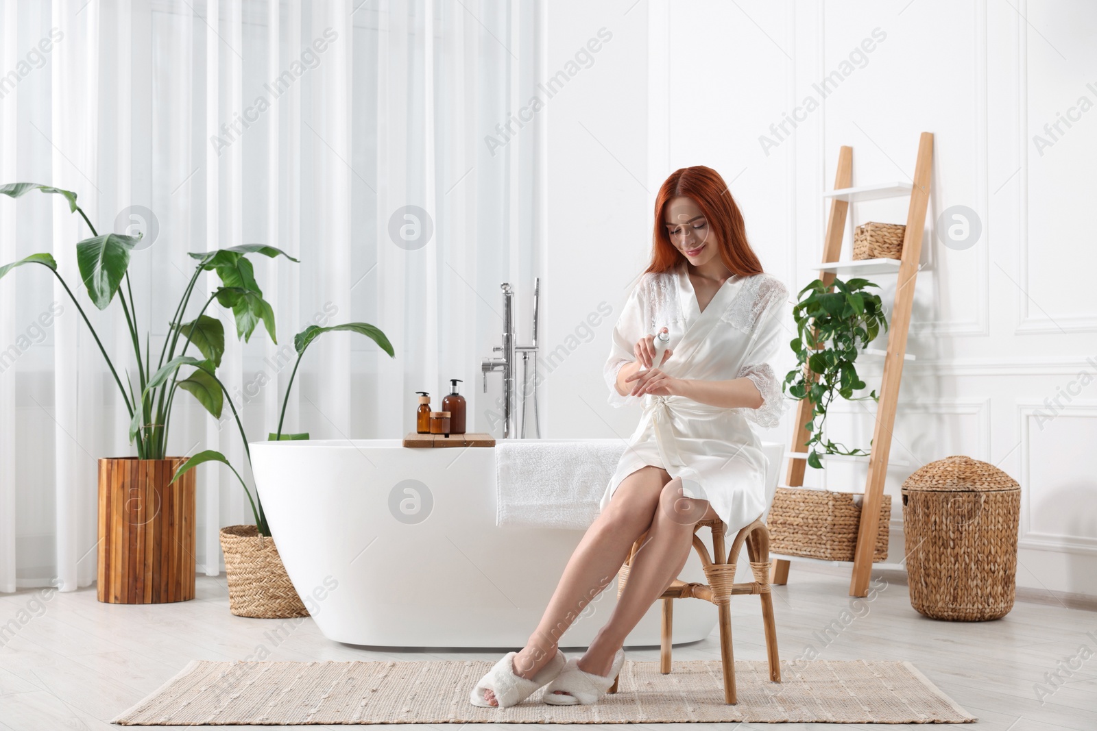 Photo of Beautiful young woman applying body spray onto hands in bathroom, space for text