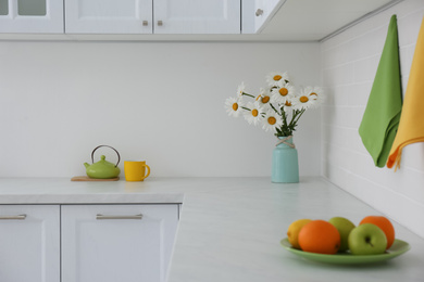 Photo of Beautiful bouquet, fruits and tea set on counter in kitchen. Interior design