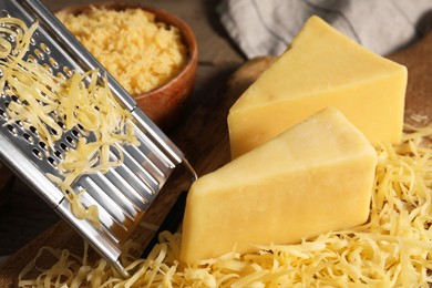 Photo of Grated, whole pieces of cheese and grater on table, closeup