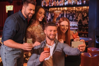 Photo of Happy friends with cocktails taking selfie together in bar