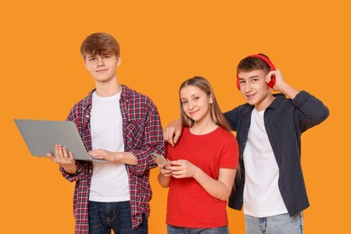 Group of happy teenagers with different gadgets on orange background