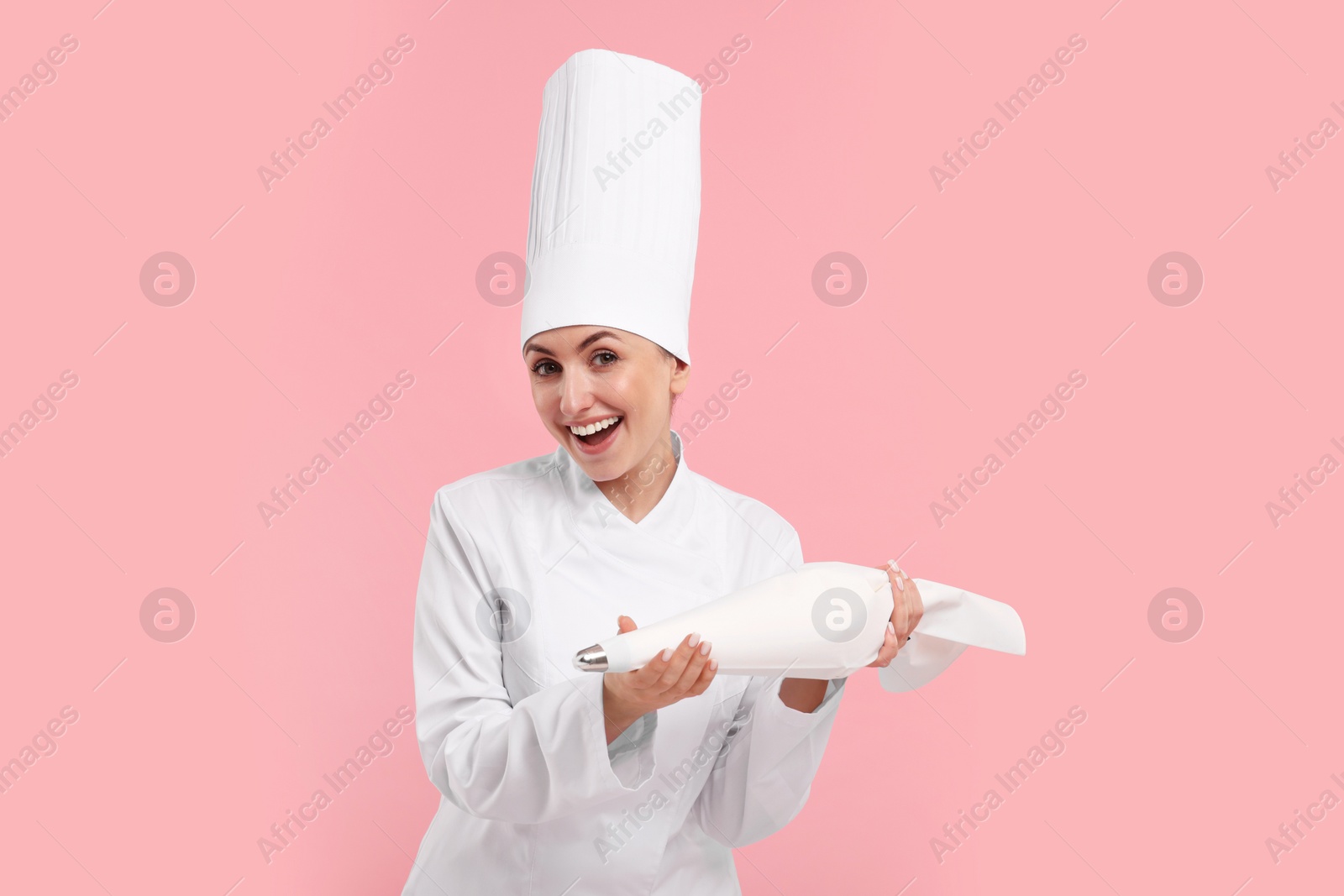 Photo of Happy professional confectioner in uniform holding piping bag on pink background