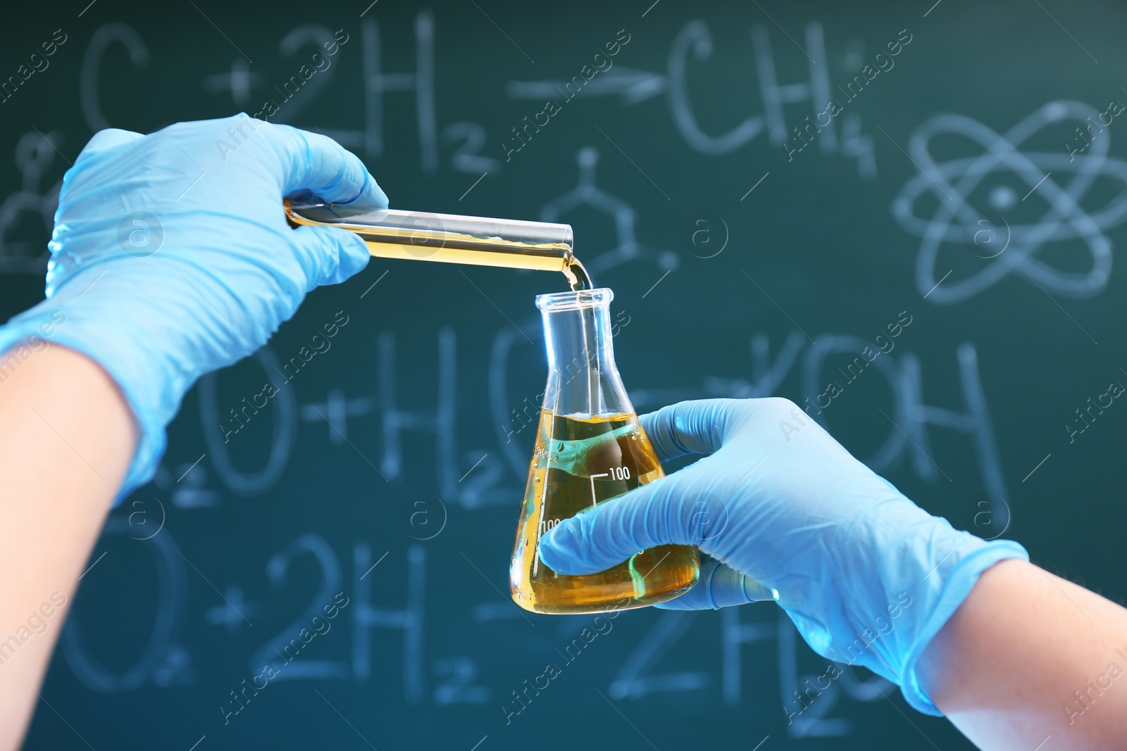 Photo of Scientist pouring liquid into flask against chalkboard, closeup. Chemistry glassware