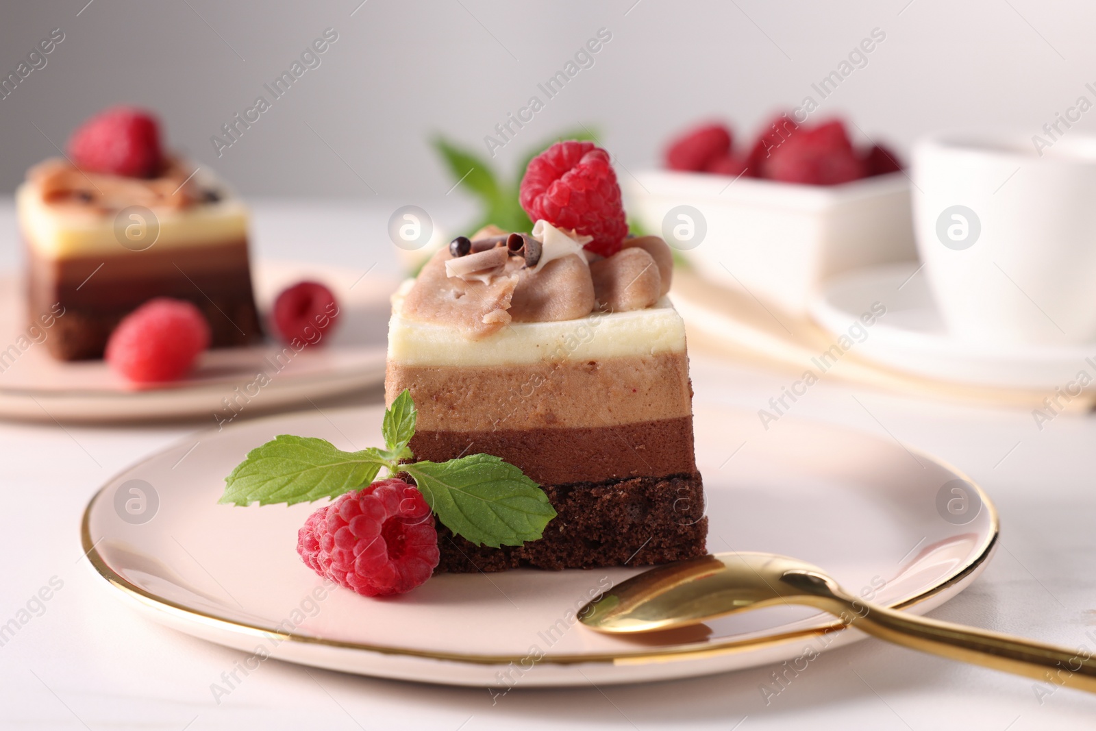 Photo of Piece of triple chocolate mousse cake with raspberries served on white table, closeup