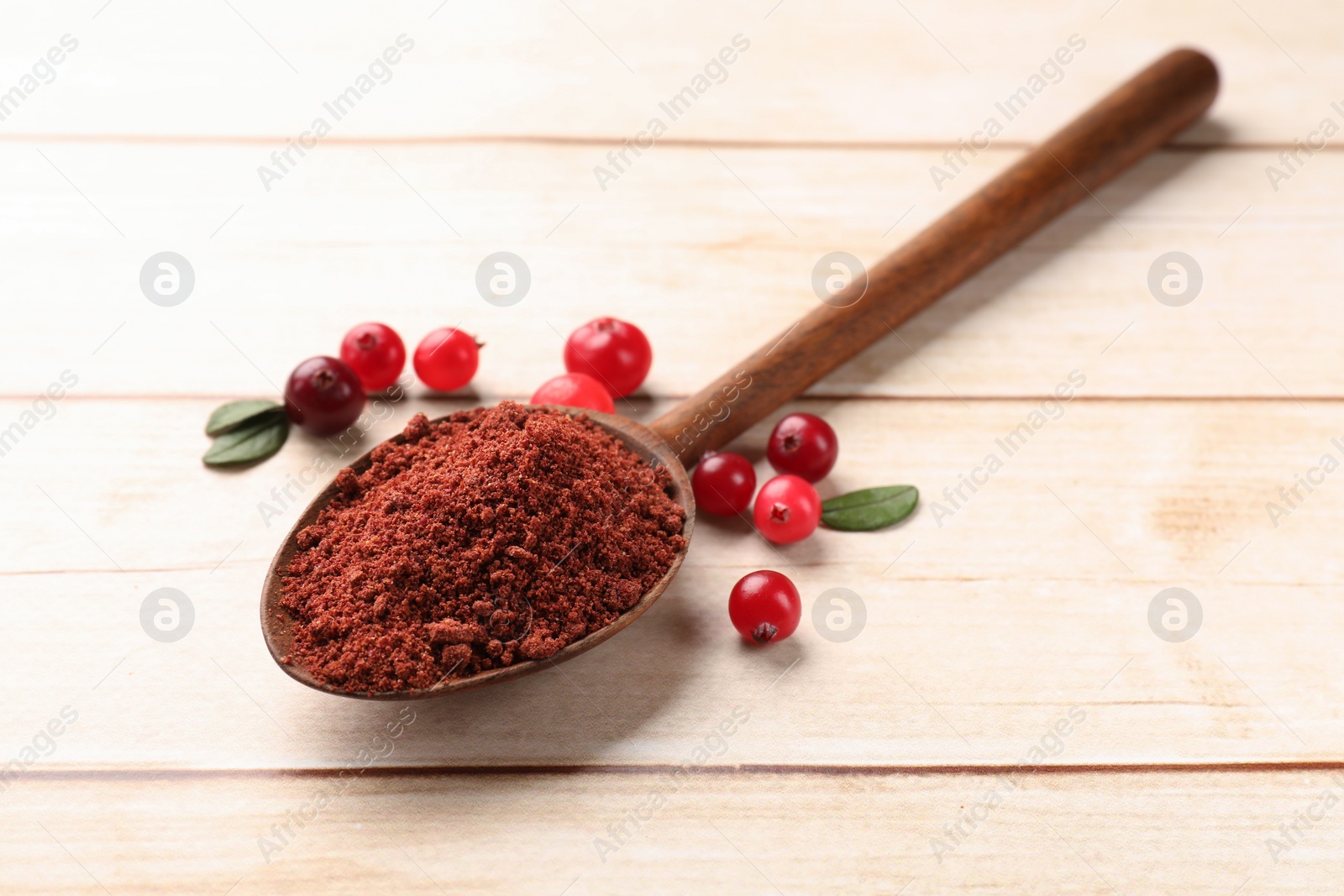 Photo of Dried cranberry powder in spoon, fresh berries and green leaves on light wooden table