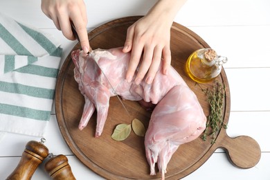 Photo of Woman cutting whole raw rabbit at white wooden table, top view