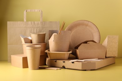 Photo of Eco friendly food packaging. Paper containers, tableware and bag on pale yellow background