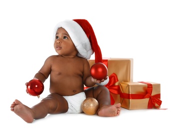 Photo of Cute African-American baby wearing Santa hat with Christmas gifts on white background