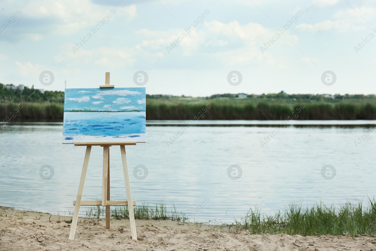 Photo of Wooden easel with unfinished painting near lake