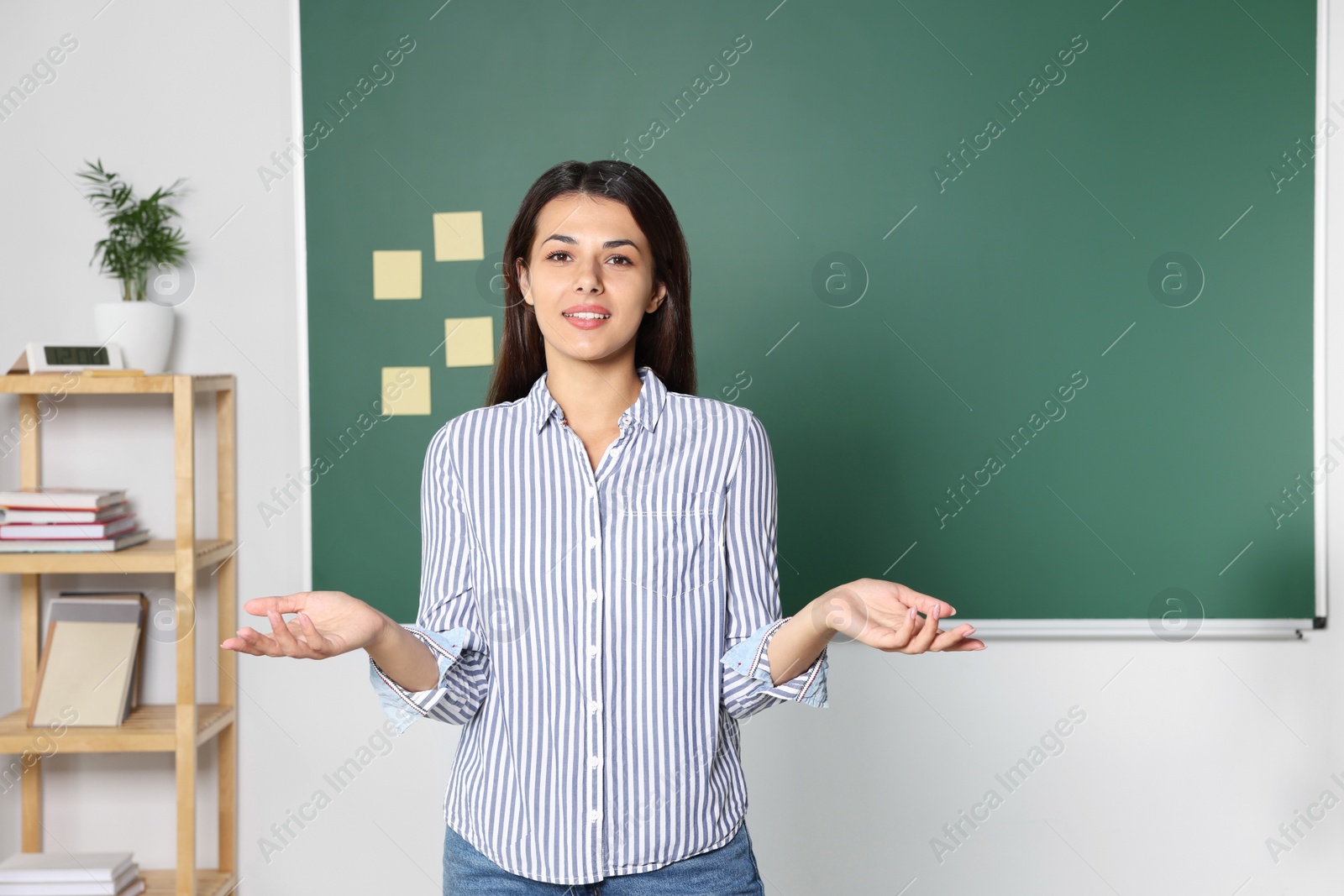 Photo of Happy young teacher giving lesson at blackboard in classroom. Space for text