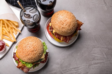 Photo of Composition with juicy bacon burgers on grey table, above view