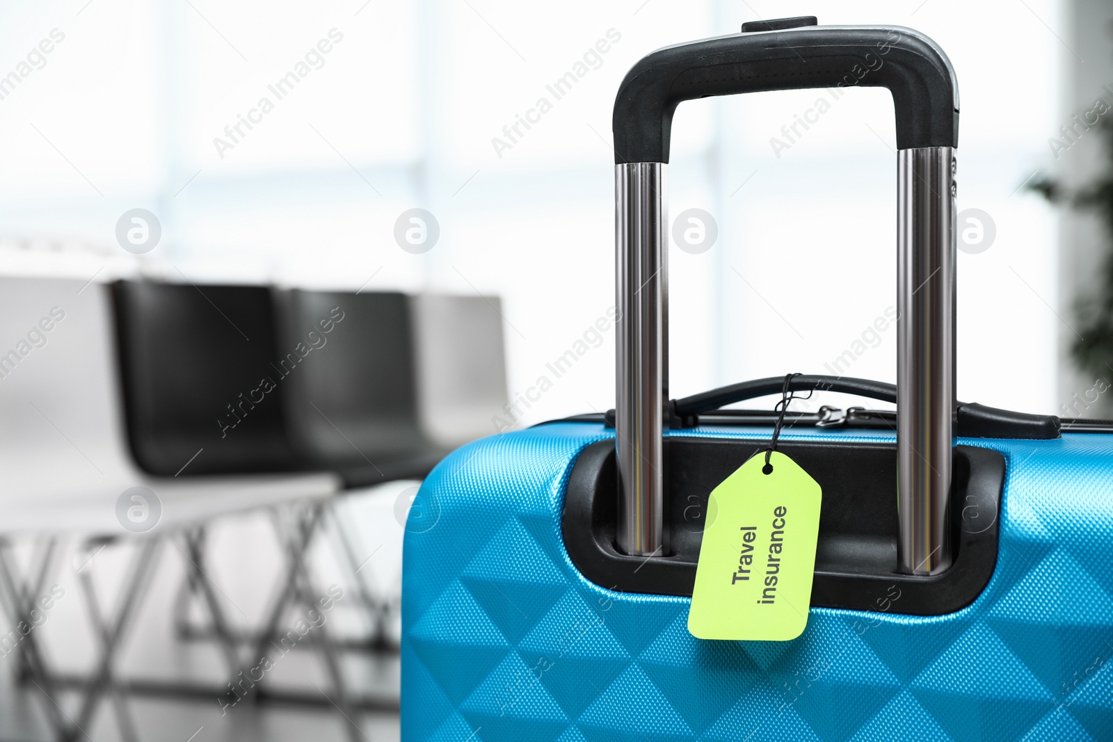 Photo of Blue suitcase with TRAVEL INSURANCE label indoors, closeup. Space for text