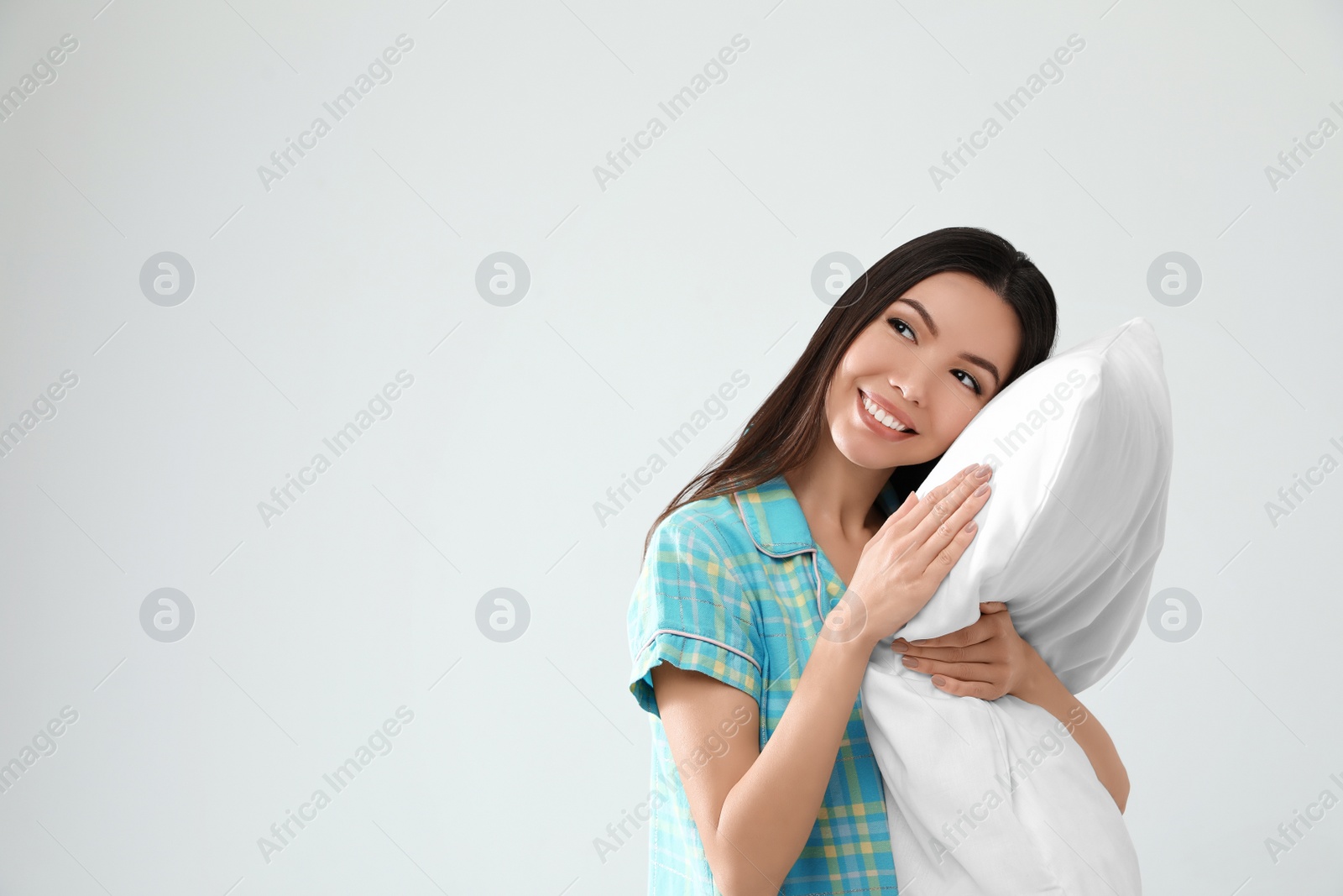 Photo of Beautiful Asian woman with pillow on light grey background, space for text. Bedtime