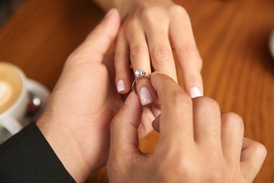 Photo of Man putting engagement ring on his girlfriend's finger in cafe, closeup