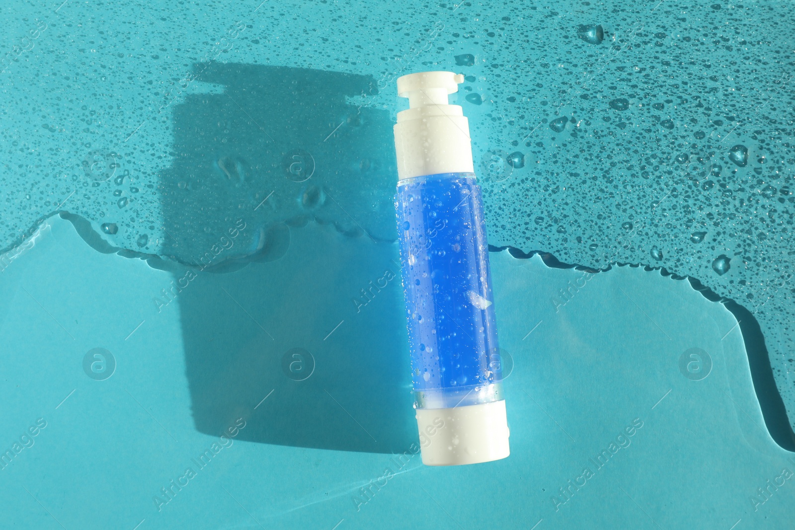 Photo of Bottle of cosmetic product in water on turquoise background, top view