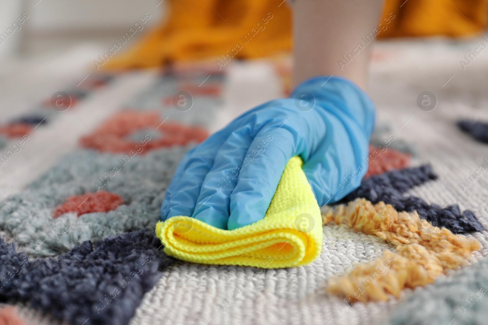 Photo of Woman in rubber gloves cleaning carpet with rag indoors, closeup