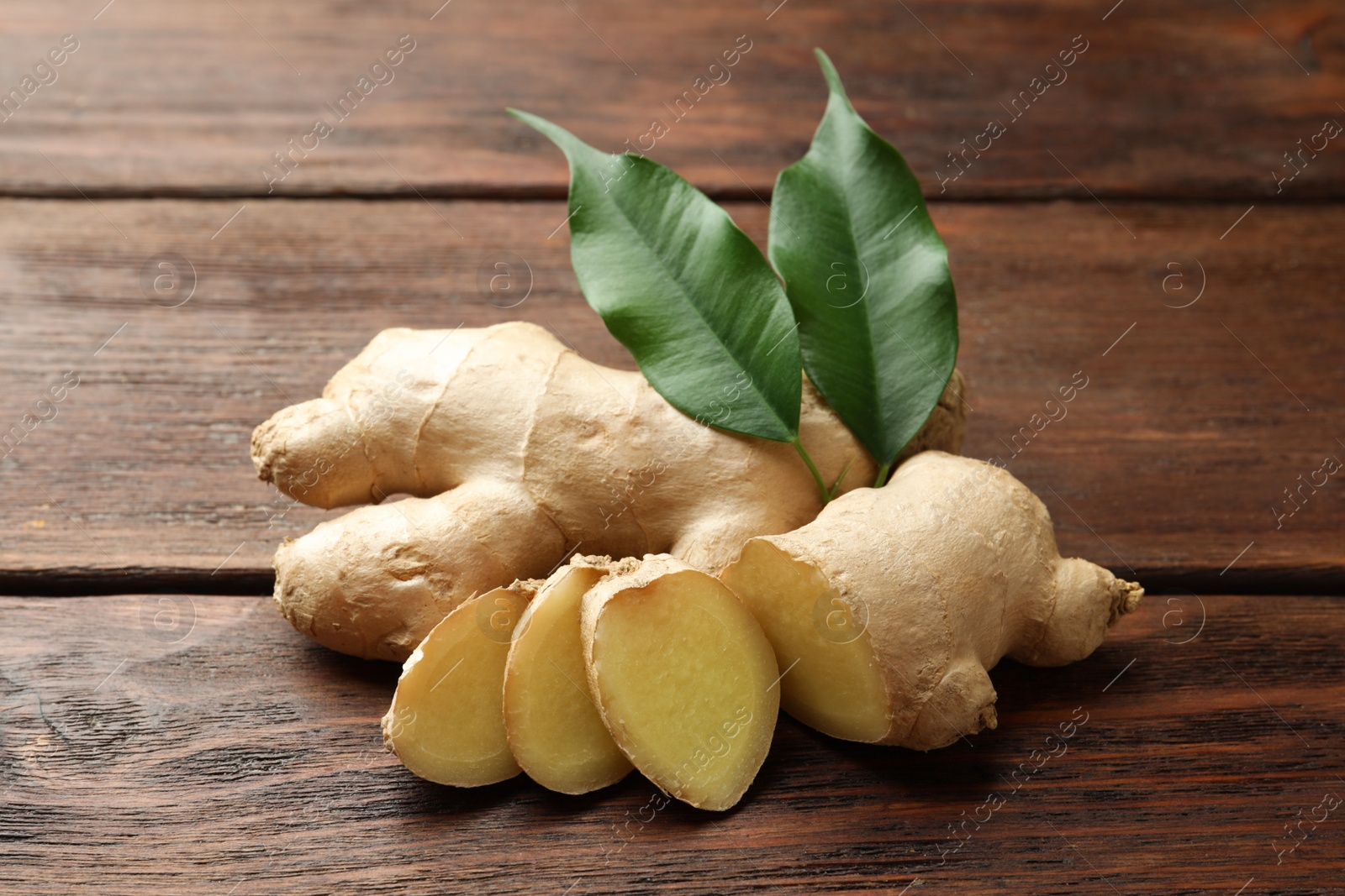 Photo of Cut and whole fresh ginger with leaves on wooden table