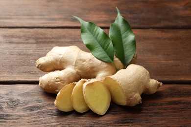 Photo of Cut and whole fresh ginger with leaves on wooden table