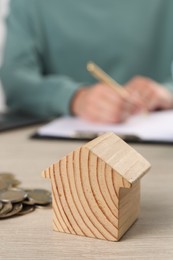 Woman planning budget at wooden table, focus on house model