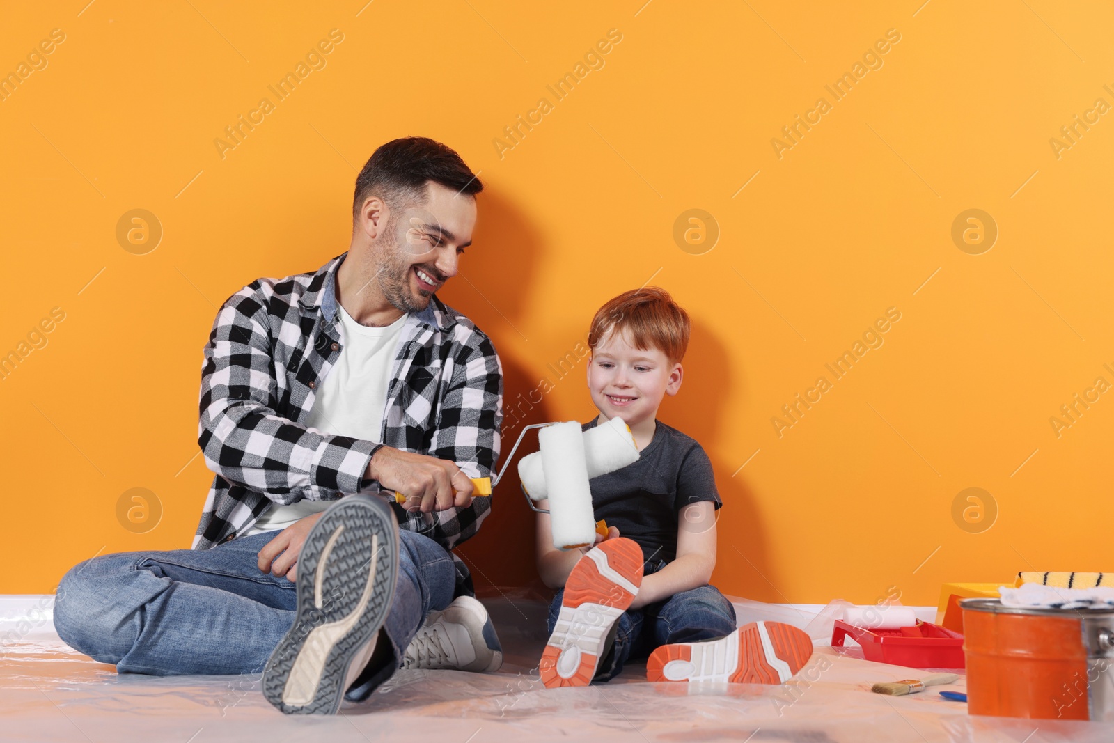 Photo of Father and son with rollers near orange wall. Repair work