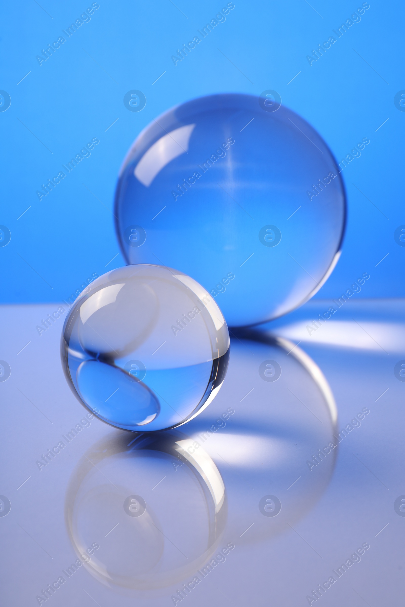 Photo of Transparent glass balls on mirror surface against blue background